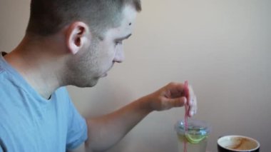 Bir adam karışımı paket servis bardağıyla karıştırıyor. Misafir, sarı bir duvarın arkasında pipetle narenciyeyle içkisini içiyor.