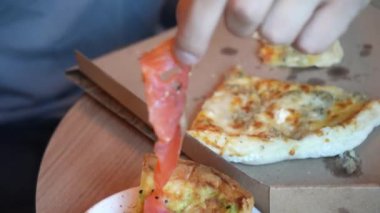 Yeni teslim edilmiş bir pizza karton bir kutunun üzerinde masanın üzerinde yatıyor. Pizza dilimlerini kapatın. Fırınlanmış ürünleri yiyen bir adam.