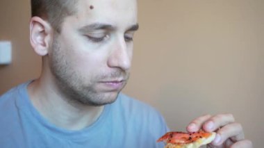 Sıradan bir yemek, bir adam bir kafede bir dilim pizzadan bir ısırık aldığında. Bir adam elinde bir dilim pizza tutar, onu ağzına koyar ve tadını çıkartır.