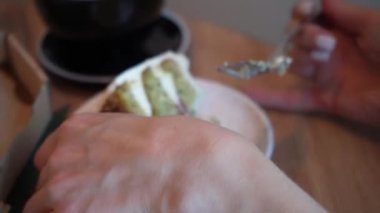 Süt manikürlü kadın eller küçük bir tatlı tabağı ve bir pasta alır. Tahta masada tatlı ve kahve var.