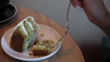 Beyaz kremalı bir parça kek kırılır ve bir el çatalı içine sokar. Tahta masada bir tatlı tabağı var.