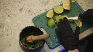 Yeşil bir tahtanın üzerinde dilimlenmiş limon ve limon var. Açık mutfak yüzeyinde siyah bir seramik kase duruyor. Malzemeleri bir konteynıra dökme süreci