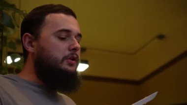 Koyu saçlı, sakallı genç bir adam restoranda sipariş bekliyor, yakın plan. Yarı romantik ve çok hoş bir atmosfer.