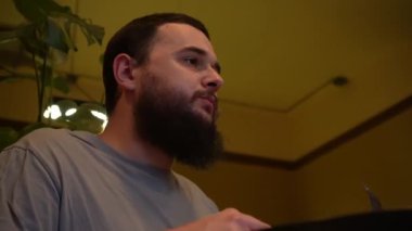 Koyu saçlı, sakallı genç bir adam restoranda sipariş bekliyor, yakın plan. Yarı romantik ve çok hoş bir atmosfer.