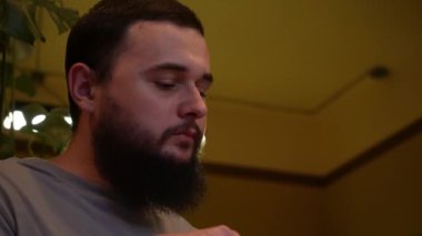 Koyu saçlı, sakallı genç bir adam restoranda sipariş bekliyor, yakın plan. Yarı romantik ve çok hoş bir atmosfer.