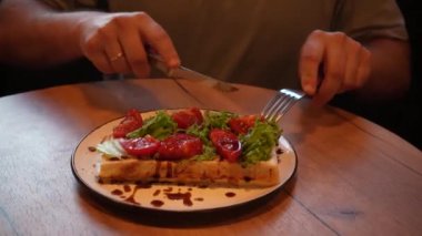 Odak noktası eller, tabaklar ve parlak yiyecekler. Sıcak bir atmosferde sağlıklı yiyecekler sergiliyorlar. Bir adam taze sebzeler, domatesler ve taze Belçika wafflelarından oluşan lezzetli bir tabak keser.