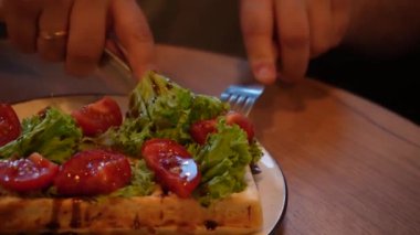 Bir adam taze sebzeler, domatesler ve taze Belçika waffle 'ı ile lezzetli bir yemek keser. Odak noktası eller, tabaklar ve parlak yiyecekler. Sıcak bir atmosferde sağlıklı yiyecekler sergiliyorlar.