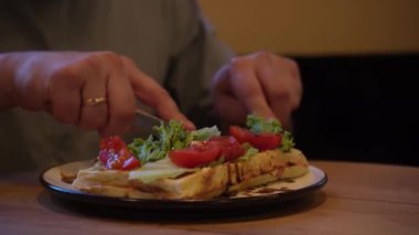 Tabak, rahat bir atmosferde sağlıklı yiyecekleri ön plana çıkaran ahşap bir masada servis ediliyor. Yakından bakınca, çatal ve bıçakla taze domates salatası yiyen bir adam görülüyor.