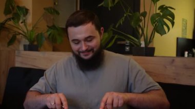 Loş bir kafede, ahşap bir masada yemek yiyen sakallı bir adamın yakın çekimi. Yumuşak atmosfer ve erkeğin yemeklerine yoğunlaşması, tek başına huzurlu bir yemek anının basitliğini vurgular.