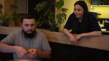 Uzun siyah saçlı genç bir kız oğlanın yanında duruyor ve tatlı tatlı sohbet ediyorlar. Bir adam bir kafede masada oturmuş, emirlerini bekliyor.