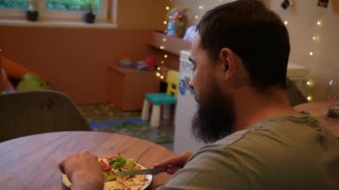 Sakallı bir adam yemek yemekten zevk alır, yemek tabağına odaklanır. Sıcak bir ışık ve sakin bir atmosfer etrafını sarar. Uzun bir günün ardından gevşemek için mükemmel bir yemek deneyimi yaratır.