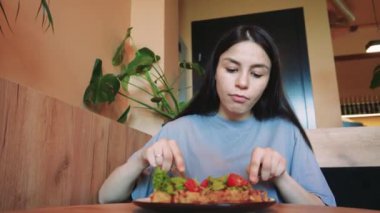 Genç bir kadın pencerenin yanında yemeğin keyfini çıkarırken sıradan bir yemek anı. Sakin atmosfer, doğal ışık ve sağlıklı besinlerle, bir denge ve refah hissi yakalar.