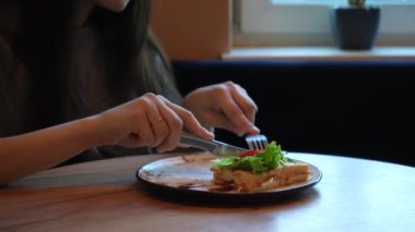 Gündelik giyinmiş bir kadın yemeğini düşünceli bir şekilde ev ortamında yer. Parlak gün ışığı penceresinden süzülüp sağlıklı yiyeceklerinin tazeliğini vurguluyor.