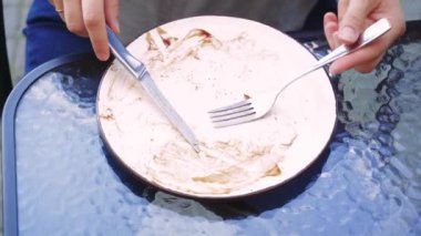 Arka planda doğal ışık ve yeşillik sakin ve taze bir atmosfer yaratır. Dışarıda sağlıklı bir yemeğin tadını çıkaran genç bir kadın çatal ve bıçakla yemek yerken tabağına odaklanmış.