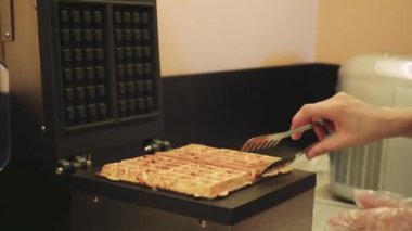 Bir kadın hamuru bir waffle makinesinde pişirir ve hamuru güzelce pişirmek için waffle 'ı transfer eder. Sahne sağlıklı ev yemeklerine ve düzgün mutfak işlerine odaklanıyor.