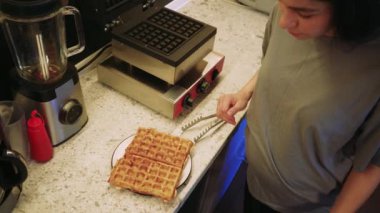 Bir çift yeni pişmiş Belçika waffle 'ı beyaz bir tabakta oturup altın gevrekliklerini sergiliyor. Video, bu klasik kahvaltı ikramının lezzetli sunumunu kaydediyor.