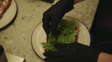 Süreç, ev yemeği ve sağlıklı malzemelerin kombinasyonunu gösteriyor. Genç bir kadın mutfakta lezzetli waffle hazırlıyor, üzerine taze marul ve domates ekliyor.