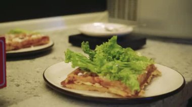 Yeşil salata ve domatesle waffle hazırlayan genç bir kadının detaylı görüntüleri. Görüntü, profesyonel bir mutfakta ev yapımı yemeğin ve düzgün beslenmenin tadını vurguluyor. Yüksek kalite fotoğraf