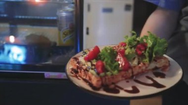 Bir kız taze yeşil yapraklı ve lezzetli kırmızı vişneli domatesli Belçika waffle 'ı gösteriyor. Pastırmalı ve peynirli taze pişmiş tuzlu waffle.