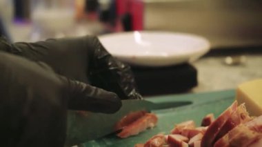 Kız lezzetli bir tat için ustaca pastırma ve peynir ekliyor, her seferinde aşçılık yeteneklerini gösteriyor. Kız yeşil bir mutfak tahtasında sert peynir ve jambon kesiyor.