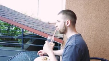 Sükunet anında yakalanan bir adam, içkisiyle yalnız başına dinlenir. Temiz bardak, serinletici içeceği vurguluyor.