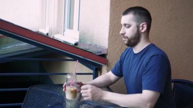 Sükunet anında yakalanan bir adam, içkisiyle yalnız başına dinlenir. Temiz bardak, serinletici içeceği vurguluyor.