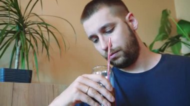 Genç bir adam güneşli bir günde kafede ferahlatıcı bir kokteylle rahatlar. Odadaki rahat atmosfer bu huzurlu yaz resmini tamamlıyor.