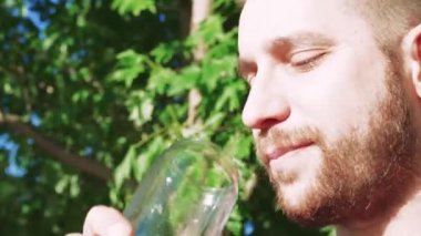 Serin bir kokteyl yudumlayan bu genç adam dışarıda mola veriyor. Etrafı canlı yaz yapraklarıyla çevrili, yazın ferahlatıcı tadını kucaklıyor.