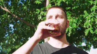 Serin bir kokteyl yudumlayan bu genç adam dışarıda mola veriyor. Etrafı canlı yaz yapraklarıyla çevrili, yazın ferahlatıcı tadını kucaklıyor.