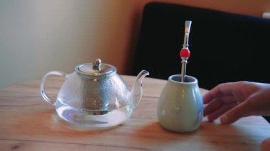 Bir adamın beyaz seramik bardaktan metal bir pipetle çay içtiği sıradan bir an. Arka planda demlik buharı