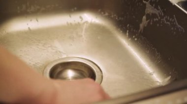 Mutfakta bulaşık yıkayan biri, akan suyun altında parlak metal bir lavaboyu temizler. Resim günlük ev ödevlerini iş başında gösteriyor