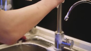 Bir çift el paslanmaz çelik mutfak yüzeyini sabit bir akıntı altında süngerle yıkıyor. Mutfak bakımının basit ama önemli bir parçası.