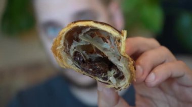 Video, genç bir adamın siyah tahtada yeni kesilmiş bir kruvasana nazikçe dokunuşunu gösteriyor. Koyu arkaplanın kontrastı kruvasanın tuhaf ve davetkar dokusunu vurgular.