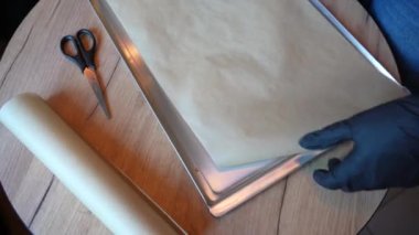Eldivenli bir el pişirme parşömenini keser ve pişirme hazırlığı için de bir tava. Hamur hazırlama süreci