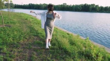 Etrafı yeşilliklerle çevrili bir kadının nehir boyunca sessiz bir yürüyüş yaptığı sakin bir sahne. Doğa, yaşam tarzı ve rahatlama temalı görseller için mükemmel.