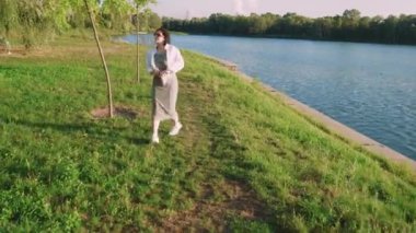 Gün batımında sakin bir nehir kenarı yürüyüşü bir kadının doğanın dinginliğinden hoşlanması gibi. Huzur, doğa ve rahatlama temaları için harika.