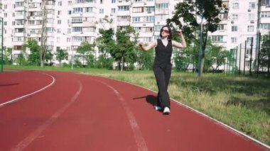 Spor sahası olan bir apartman kompleksinin yanından geçen güneş gözlüklü genç bir kadın avlunun huzuru ile çevrili bir şekilde düşüncelere daldı..