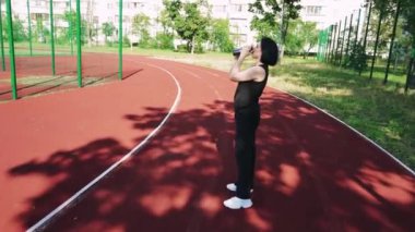 Şehir hayatı ve sessiz düşüncenin bir kombinasyonu. Genç bir kadın elinde bir fincan çay tutarken özenle arka planda duran spor sahası olan bir konut binasının önünde duruyor.