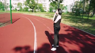 Şehir hayatı ve sessiz düşüncenin bir kombinasyonu. Genç bir kadın elinde bir fincan çay tutarken özenle arka planda duran spor sahası olan bir konut binasının önünde duruyor.