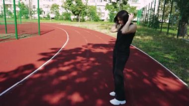 Siyah kulaklıklı genç bir kadın spor sahasında müzik dinliyor. Temiz havadaki kızın dinlenmesi ve dinlenmesi.