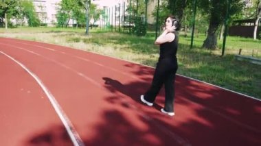 Siyah kulaklıklı genç bir kadın spor sahasında müzik dinliyor. Temiz havadaki kızın dinlenmesi ve dinlenmesi.