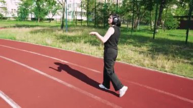 Siyah kulaklıklı genç bir kadın spor sahasında müzik dinliyor. Temiz havadaki kızın dinlenmesi ve dinlenmesi.