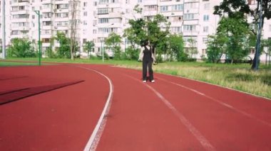 Siyah giyinmiş genç bir kadın spor sahasında yürüyor. Çalışma gününden sonra aktif dinlenme için ideal