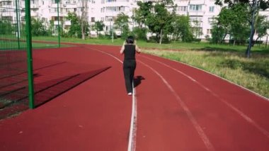 Siyah giyinmiş genç bir kadın spor sahasında yürüyor. Çalışma gününden sonra aktif dinlenme için ideal