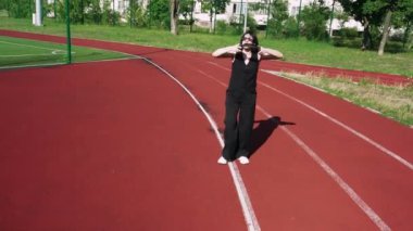 Yeşil ve yüksek binaların yakınında kırmızı bir pistte yürüyen bir kadın, şehir manzarası ve aktif yaşam tarzı görselleri için ideal.