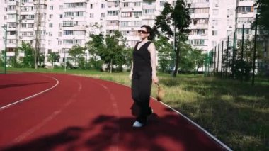 Arka planda şehir binaları olan kırmızı bir pistte güvenle yürüyen bir kadın. Şehir yaşam tarzı ve fitness ile ilgili konular için mükemmel