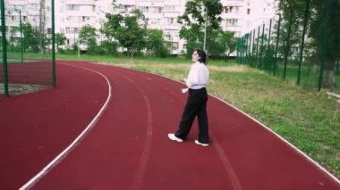 Arka planda şehir binaları olan kırmızı bir pistte güvenle yürüyen bir kadın. Şehir yaşam tarzı ve fitness ile ilgili konular için mükemmel