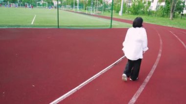 Arka planda şehir binaları olan kırmızı bir pistte güvenle yürüyen bir kadın. Şehir yaşam tarzı ve fitness ile ilgili konular için mükemmel