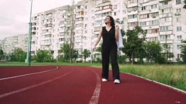 Arka planda apartmanlar ve yeşil ağaçlar var. Günün ortasında, siyah pantolonlu bir kız spor egzersizleri için oraya yürüyordu.