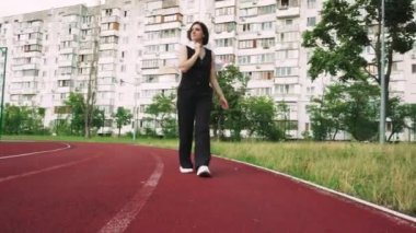 Arka planda apartmanlar ve yeşil ağaçlar var. Günün ortasında, siyah pantolonlu bir kız spor egzersizleri için oraya yürüyordu.
